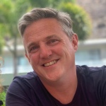 Alex Prichard: Alex is smiling and wearing a dark-coloured top. He has short grey hair.