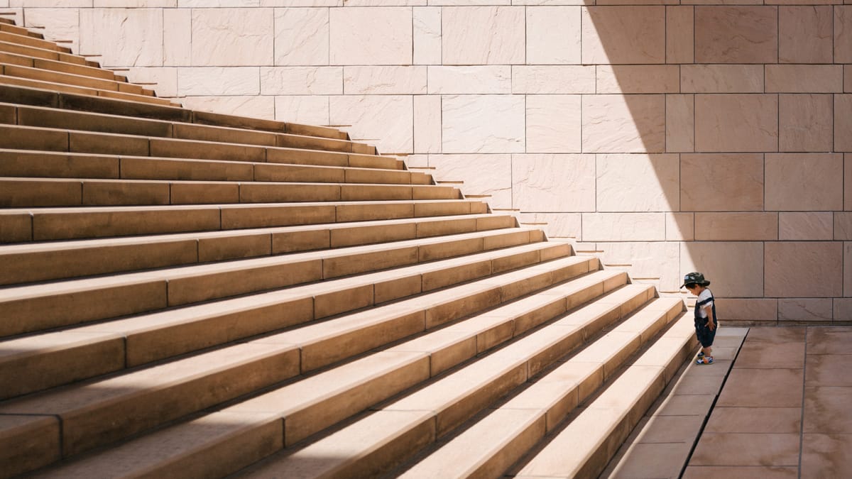 Picture of a small child staring at a big staircase about to climb it.