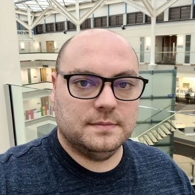 Matt Barnard - Matt is standing in an atrium. He's wearing black glasses and a dark-coloured top